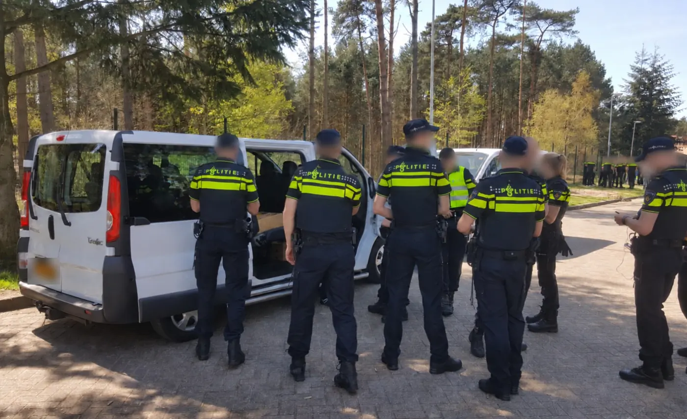 Een groep agenten bij een politiebus tijdens een praktijktraining op een oefenterrein